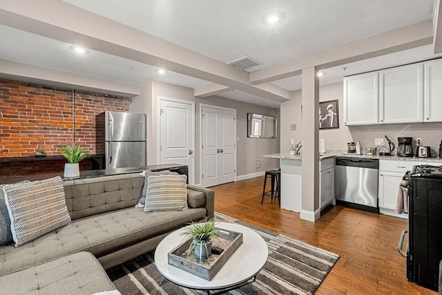 living room with baseboards, recessed lighting, brick wall, and wood finished floors