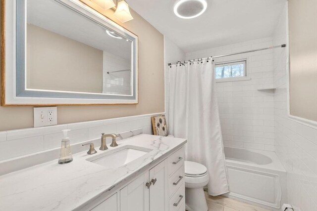bathroom with vanity, shower / bathtub combination with curtain, a wainscoted wall, and toilet