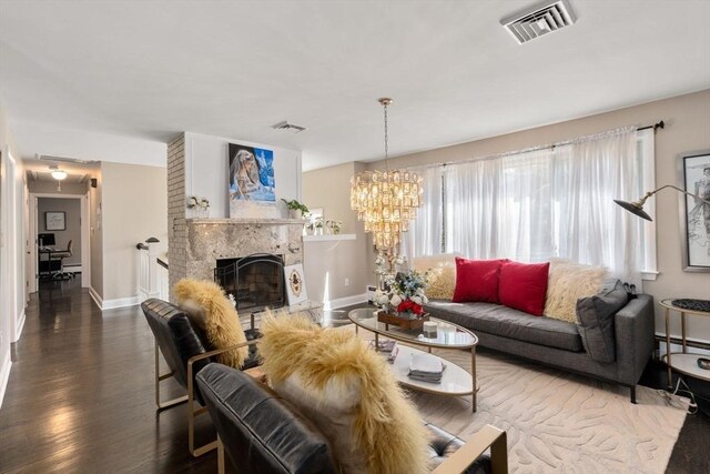 living area with a fireplace with raised hearth, baseboards, visible vents, and wood finished floors