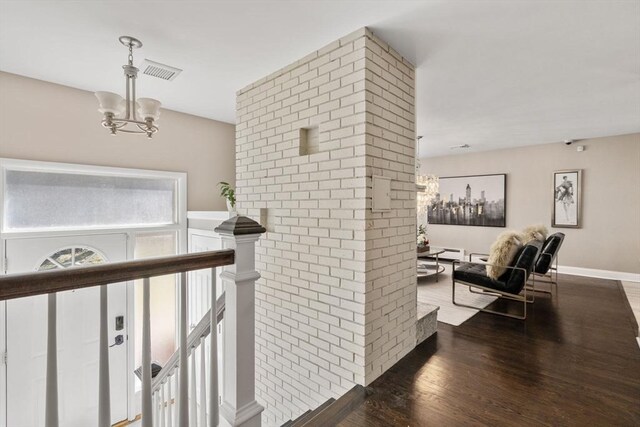 corridor featuring a chandelier, wood finished floors, visible vents, and an upstairs landing