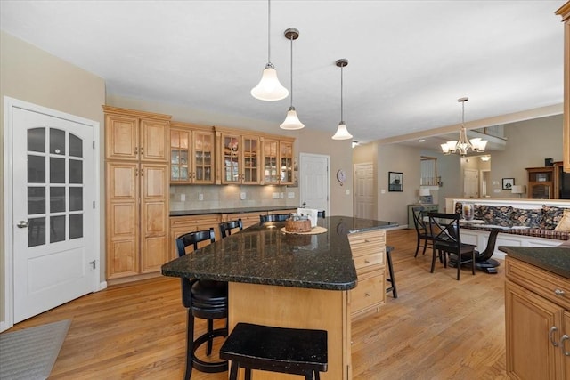 kitchen with decorative backsplash, a kitchen island, glass insert cabinets, a kitchen bar, and light wood-style flooring