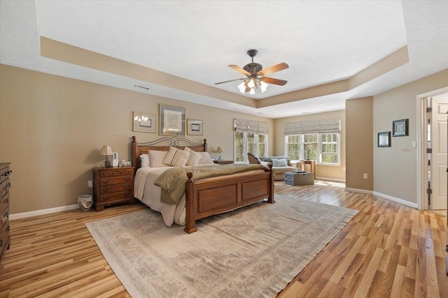 bedroom featuring a ceiling fan, baseboards, a raised ceiling, and light wood-style floors