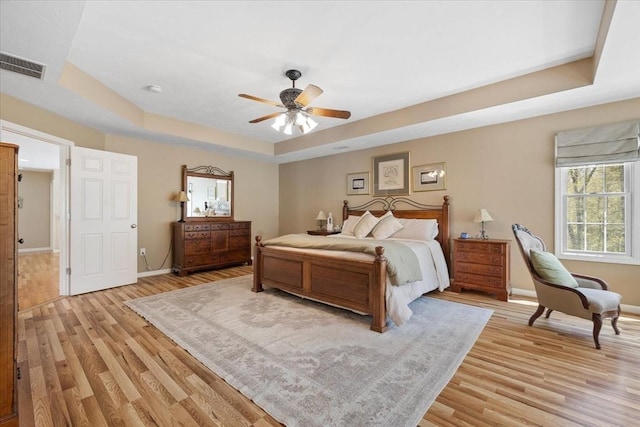 bedroom featuring a tray ceiling, visible vents, multiple windows, and light wood finished floors