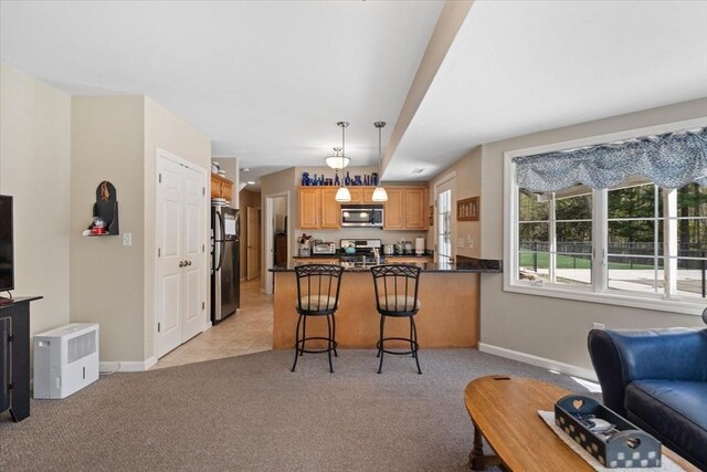 kitchen featuring appliances with stainless steel finishes, light colored carpet, a peninsula, open floor plan, and baseboards