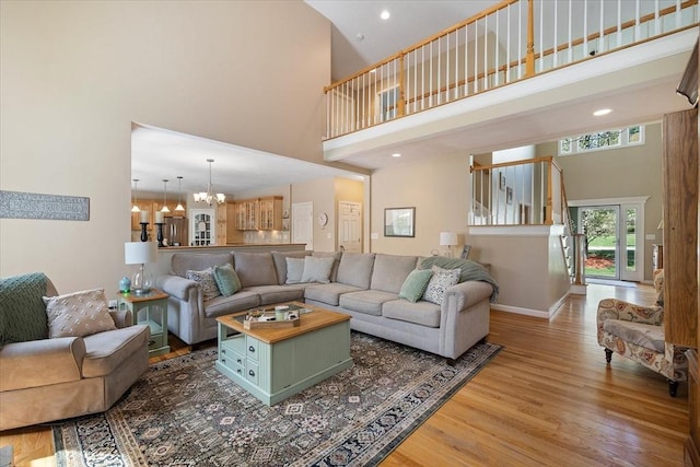 living area featuring wood finished floors, baseboards, a high ceiling, recessed lighting, and a notable chandelier
