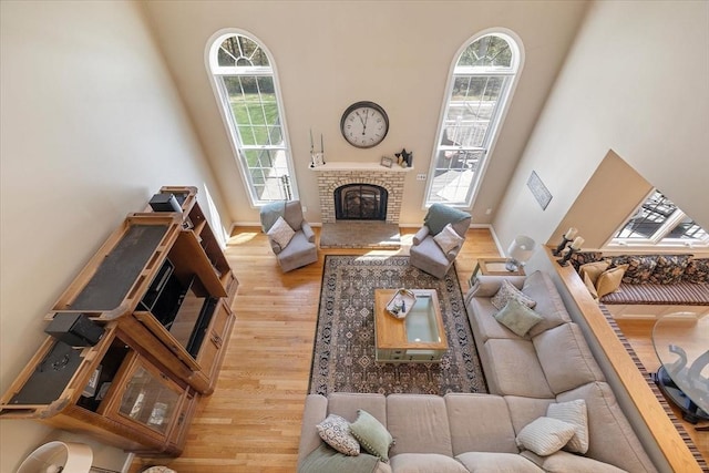 living room with baseboards, a towering ceiling, a brick fireplace, and wood finished floors