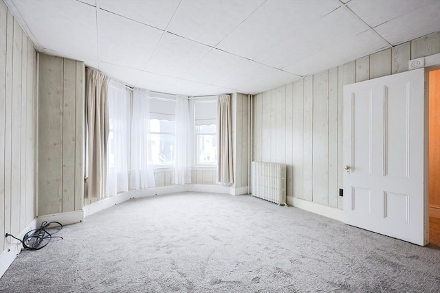 spare room featuring wood walls, radiator heating unit, and carpet flooring