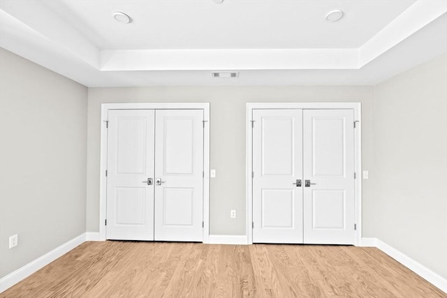 unfurnished bedroom featuring baseboards, two closets, visible vents, and light wood-style floors