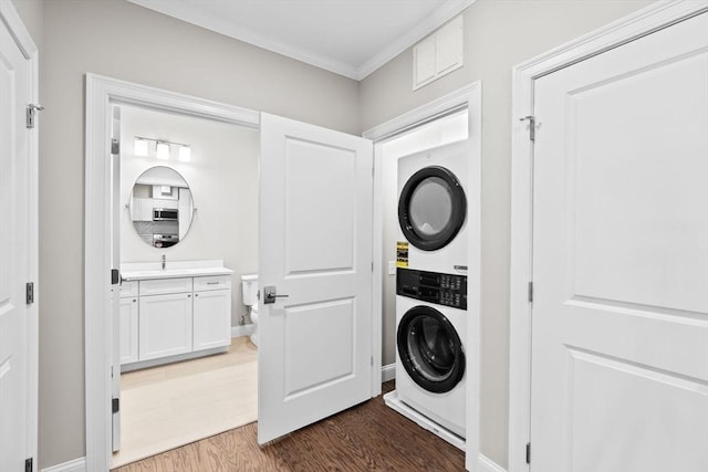 clothes washing area with crown molding, stacked washer / drying machine, visible vents, wood finished floors, and laundry area