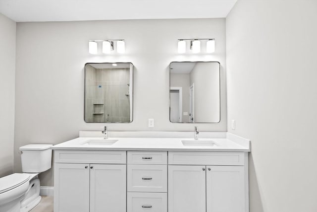 full bathroom featuring a tile shower, double vanity, a sink, and toilet