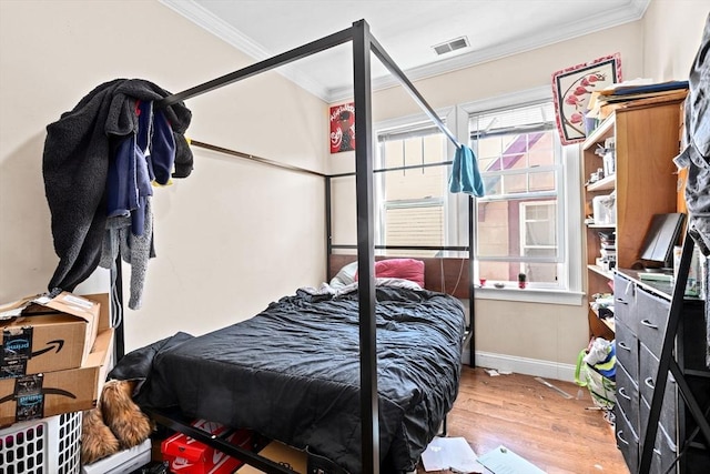 bedroom with visible vents, baseboards, crown molding, and wood finished floors