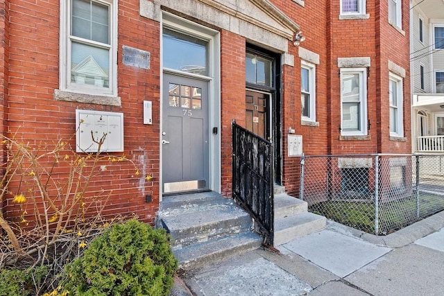 view of exterior entry featuring brick siding and fence