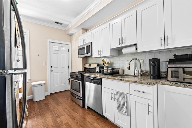 kitchen featuring a sink, appliances with stainless steel finishes, crown molding, white cabinetry, and dark stone counters