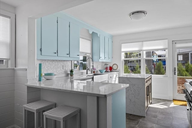 13 Selman St, Marblehead, MA 01945 - kitchen with light stone counters, blue cabinets, decorative backsplash, a peninsula, and a sink