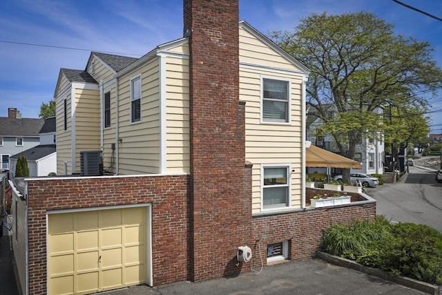13 Selman St, Marblehead, MA 01945 - view of side of property with a chimney, central AC, brick siding, and an attached garage