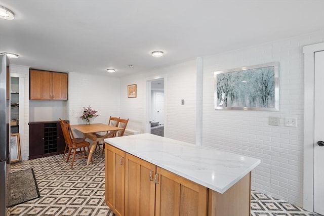 12 Temple Ave, Hudson, MA 01749 - kitchen with brick wall, light flooring, light stone countertops, a kitchen island, and brown cabinetry