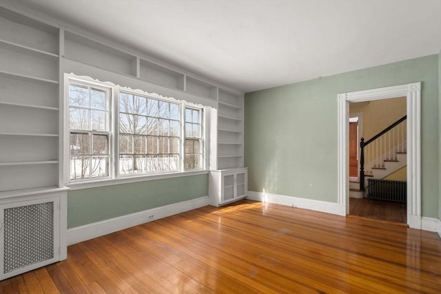 unfurnished room featuring radiator, wood-type flooring, stairs, and baseboards