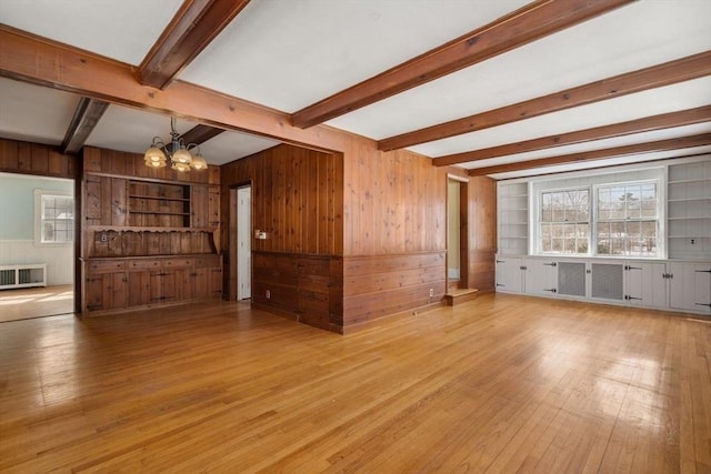 unfurnished living room with wooden walls, built in features, radiator heating unit, light wood-style floors, and a chandelier