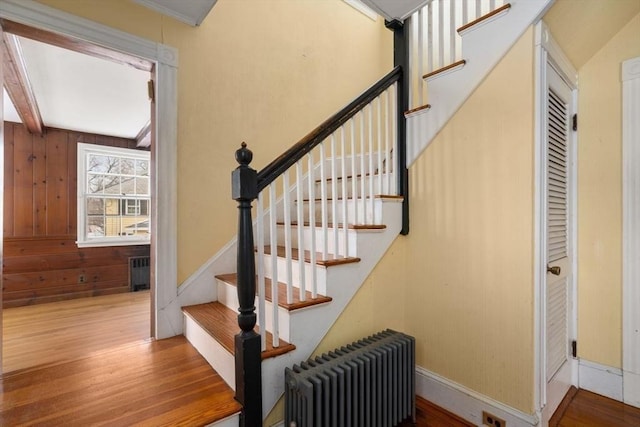 stairway featuring beam ceiling, radiator, radiator heating unit, wood walls, and wood finished floors