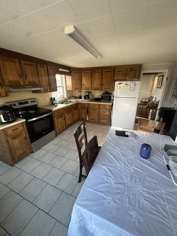 kitchen with white refrigerator, stainless steel electric stove, sink, and light tile patterned floors