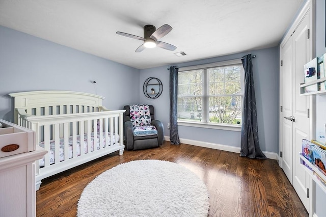 bedroom with baseboards, a crib, and wood finished floors