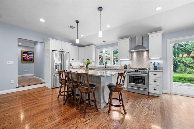 kitchen with wall chimney range hood, a healthy amount of sunlight, white cabinets, and high quality appliances