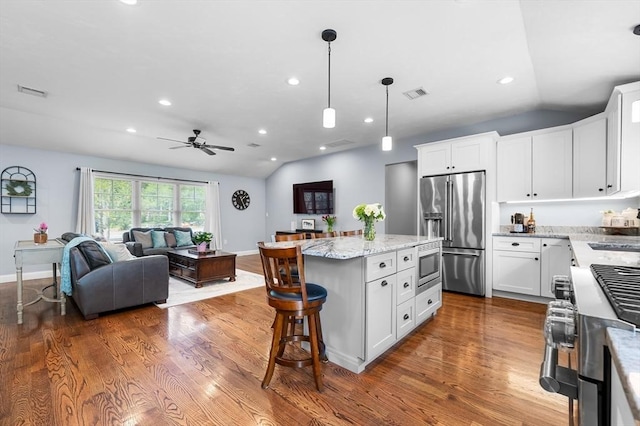 kitchen with a center island, premium appliances, visible vents, ceiling fan, and vaulted ceiling