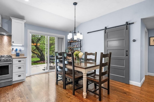 dining room with wood finished floors, a barn door, vaulted ceiling, a chandelier, and baseboards