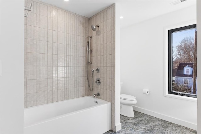 bathroom featuring tiled shower / bath combo, a healthy amount of sunlight, and toilet