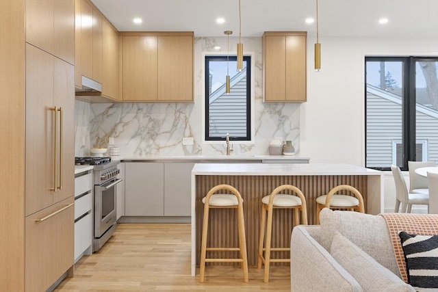 kitchen with high quality appliances, decorative light fixtures, a kitchen breakfast bar, and light brown cabinetry