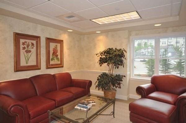 carpeted living area with baseboards, a drop ceiling, and a raised ceiling