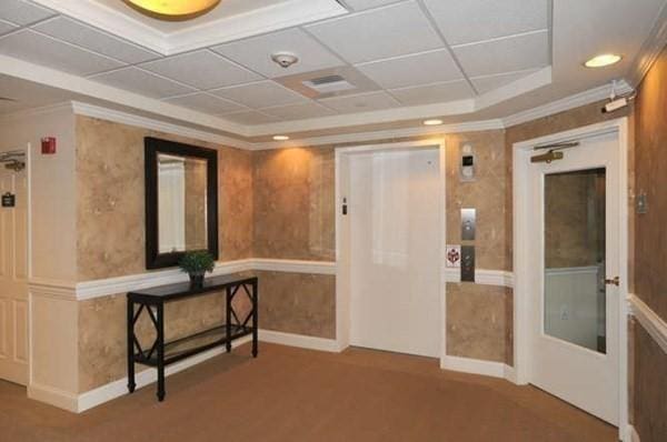 interior space with a raised ceiling, carpet, crown molding, and baseboards