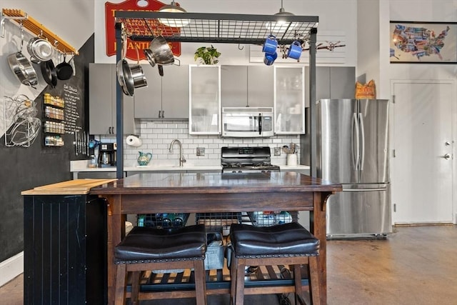 kitchen with a kitchen breakfast bar, sink, tasteful backsplash, appliances with stainless steel finishes, and concrete floors