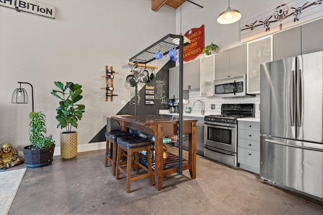 kitchen featuring concrete flooring, appliances with stainless steel finishes, gray cabinets, and tasteful backsplash