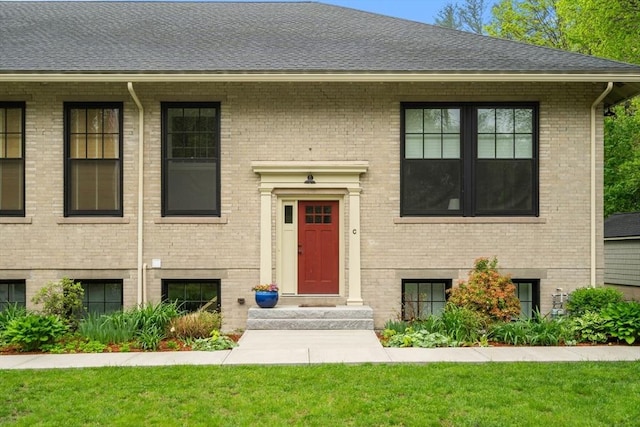 split foyer home featuring a front yard, brick siding, and roof with shingles