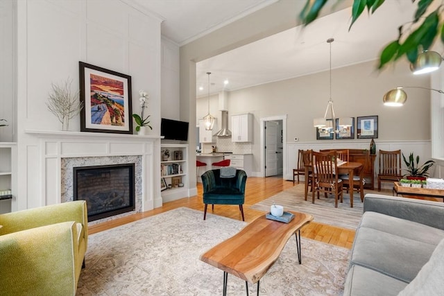living area with crown molding, light wood-type flooring, a fireplace, and a chandelier