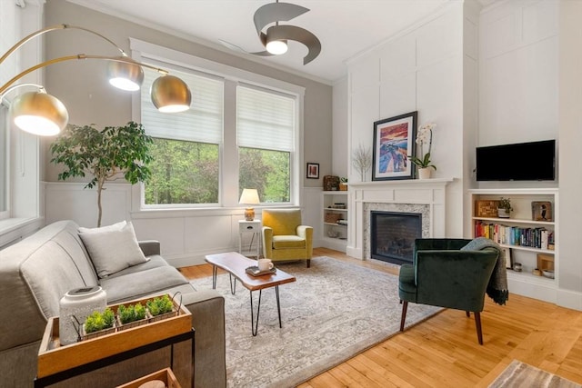 living room featuring crown molding, a premium fireplace, light wood-type flooring, ceiling fan, and built in shelves
