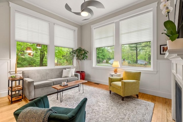 living area with a ceiling fan, wood finished floors, a fireplace, a decorative wall, and crown molding