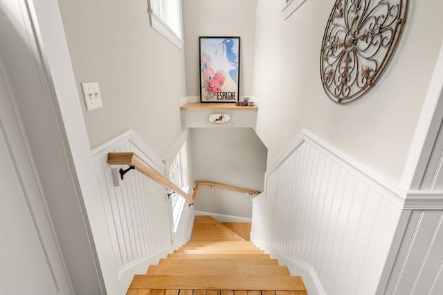 staircase featuring a high ceiling, a wainscoted wall, a decorative wall, and wood finished floors