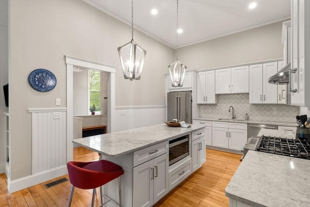 kitchen with appliances with stainless steel finishes, a sink, a center island, white cabinetry, and wainscoting