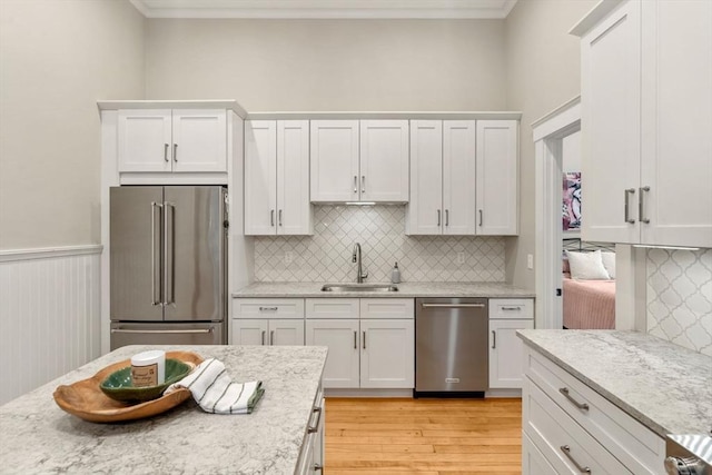kitchen featuring appliances with stainless steel finishes, a sink, light wood-style flooring, white cabinets, and backsplash