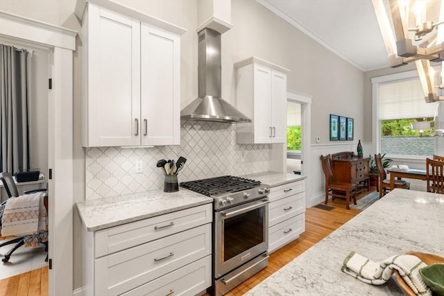 kitchen featuring high end range, wall chimney range hood, crown molding, tasteful backsplash, and white cabinets