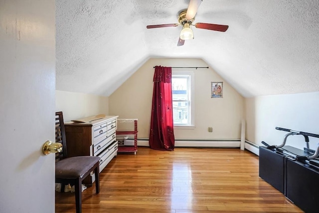 additional living space featuring a textured ceiling, vaulted ceiling, ceiling fan, hardwood / wood-style flooring, and a baseboard radiator