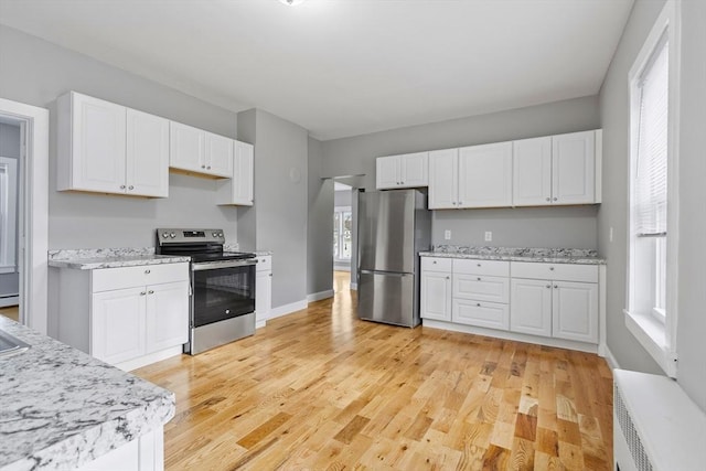 kitchen with appliances with stainless steel finishes, white cabinets, light wood-style flooring, and baseboards