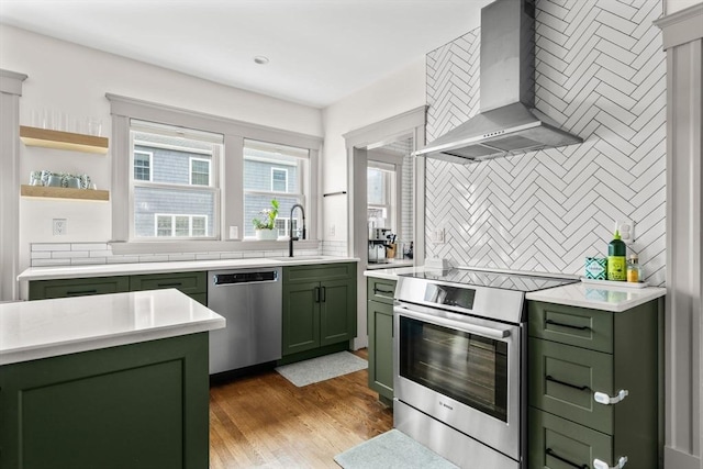 149-151 Pleasant St, Watertown, MA 02472 - kitchen with green cabinetry, wall chimney range hood, appliances with stainless steel finishes, a sink, and decorative backsplash