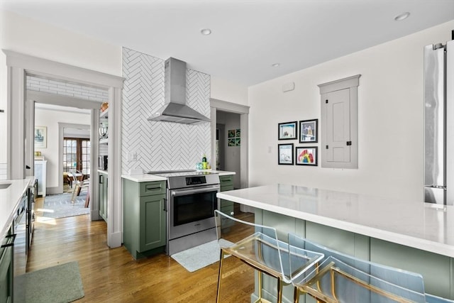 149-151 Pleasant St, Watertown, MA 02472 - kitchen featuring wall chimney exhaust hood, green cabinetry, stainless steel range with electric stovetop, light wood-style flooring, and tasteful backsplash