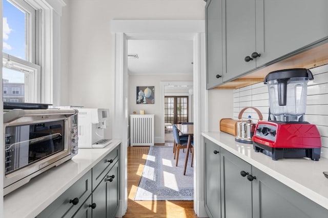 149-151 Pleasant St, Watertown, MA 02472 - kitchen featuring gray cabinets, radiator, wood finished floors, light countertops, and decorative backsplash