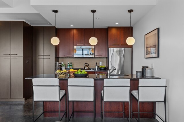 kitchen with backsplash, appliances with stainless steel finishes, dark stone counters, pendant lighting, and sink