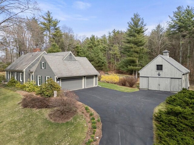 view of home's exterior with a barn, roof with shingles, a chimney, a lawn, and an outbuilding
