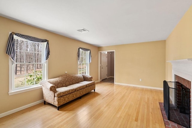 living area featuring light wood-style floors, baseboards, a brick fireplace, and visible vents